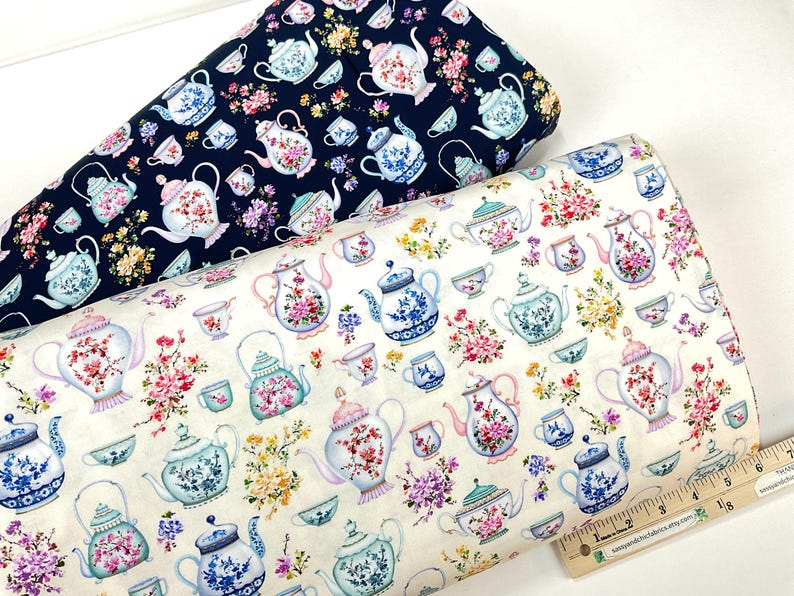 May include: Two rolls of fabric with a repeating pattern of teapots, teacups, and floral arrangements. One roll is navy blue, the other is off-white. The teapots and cups are in shades of blue, pink, and green.