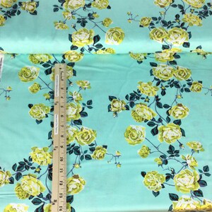 May include: A roll of fabric with a repeating floral pattern. The fabric has a light teal background with yellow roses and dark green leaves. A ruler is placed on the fabric to measure its length. The text "Love Always, AM" is visible on the edge of the fabric.