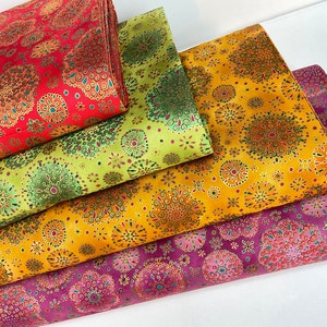 May include: Four stacks of fabric in shades of red, green, yellow, and purple. Each fabric has a repeating pattern of circular floral designs with gold accents. The fabrics are folded neatly, showcasing the variety of colors and patterns.