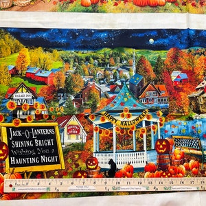 Op de afbeelding: Stoffpaneel met een Halloween-thema. De afbeelding toont een stadsgezicht met herfstbladeren, pompoenen en een prieel met een "Happy Halloween"-banner. Een bord leest "Jack-O-Lanterns Shining Bright Wishing You a Haunting Night."
