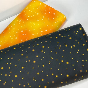 May include: Two rolls of fabric, one in a gradient of yellow and orange with white speckles, and another in black with yellow and orange dot and teardrop patterns. The fabrics are folded and angled, showcasing their designs.