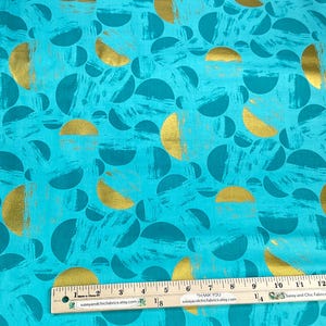 May include: Teal fabric with a gold and teal semi-circle pattern. The fabric has a textured brushstroke effect. A ruler is placed across the bottom of the fabric, measuring in inches.