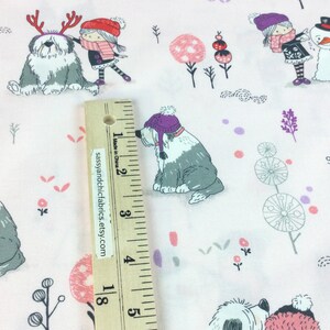 May include: Light pink fabric with a winter-themed pattern. The design features Old English Sheepdogs wearing hats and scarves, children, snowmen, and decorative trees. The fabric is decorated with small pink, purple, and gray accents.