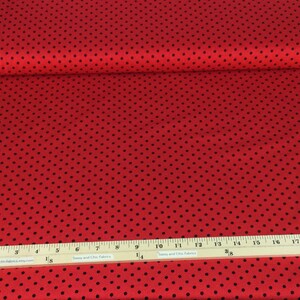 May include: Red fabric with a black polka dot pattern. A wooden ruler with inch measurements is placed on the fabric. The fabric is rolled up, showing the edge of the fabric.