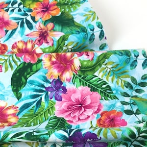 May include: Vibrant fabric featuring a tropical floral pattern. The design showcases large hibiscus flowers in shades of pink, orange, and purple, set against lush green leaves and a light blue background. The fabric is likely used for apparel or home decor.
