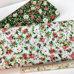 K&ouml;nnte beinhalten: Zwei Stoffrollen mit floralen Mustern. Eine Rolle hat einen gr&uuml;nen Hintergrund mit wei&szlig;en und roten Blumen. Die andere hat einen hellblauen Hintergrund mit wei&szlig;en und roten Blumen, Tannenzapfen und Beeren. Ein Lineal befindet sich unten.