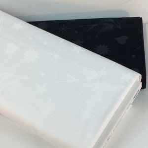 May include: Two folded fabric samples, one white and one black, are stacked. The white fabric displays a repeating pattern of birds, stars, and hearts. The black fabric has a similar design. Both fabrics appear to be cotton or a similar material.