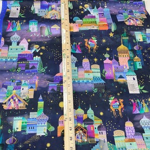 Puede incluir: Tela con un dise&ntilde;o navide&ntilde;o caprichoso que presenta edificios coloridos, estrellas y figuras. La tela tiene un fondo azul oscuro con una regla para la escala. El dise&ntilde;o incluye tonos dorados, morados, turquesas y naranjas.