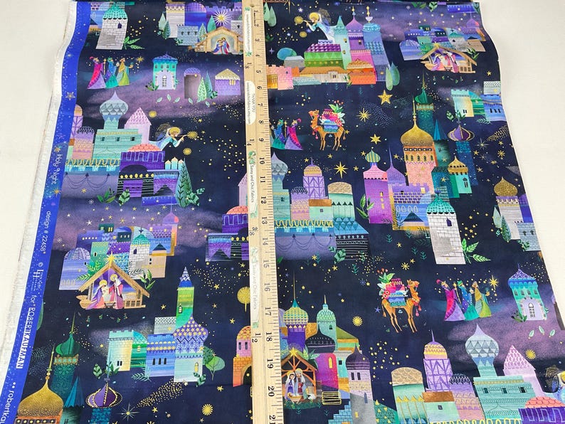 Puede incluir: Tela con un dise&ntilde;o navide&ntilde;o caprichoso que presenta edificios coloridos, estrellas y figuras. La tela tiene un fondo azul oscuro con una regla para la escala. El dise&ntilde;o incluye tonos dorados, morados, turquesas y naranjas.