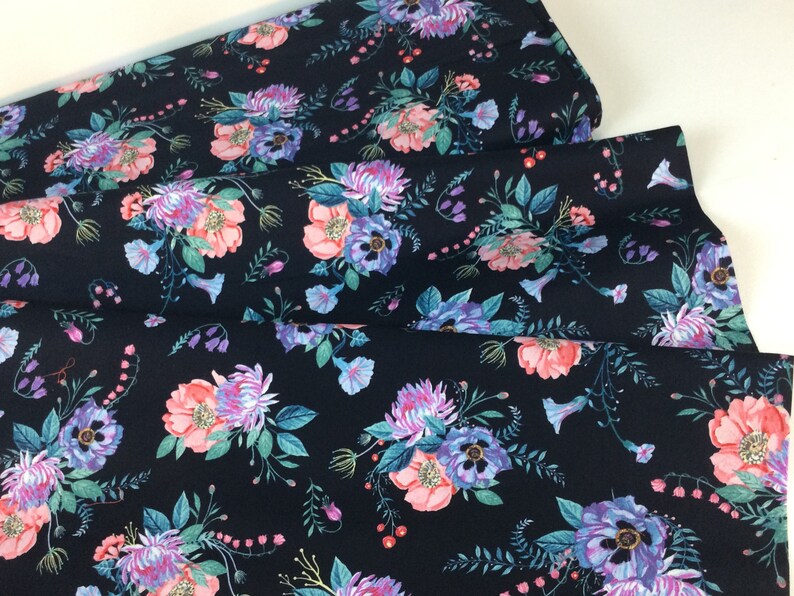 May include: Dark navy fabric with a floral pattern. The design features bouquets of pink, purple, and blue flowers with green leaves. The fabric is folded, showing the pattern's repeat.