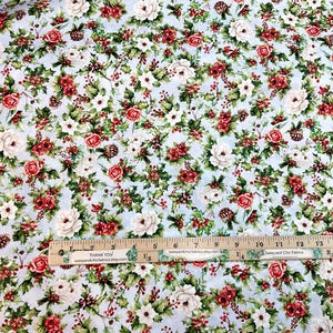 K&ouml;nnte beinhalten: Blumenstoff mit hellblauem Hintergrund, mit einem Muster aus roten und wei&szlig;en Rosen, gr&uuml;nen Bl&auml;ttern und kleinen Tannenzapfen. Ein Holzlineal mit Zollma&szlig;en ist sichtbar.