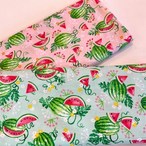 May include: Two fabric pieces with a watermelon pattern. One is light pink, the other is light blue-green. Both feature green watermelons, red watermelon slices, and white and yellow floral accents.