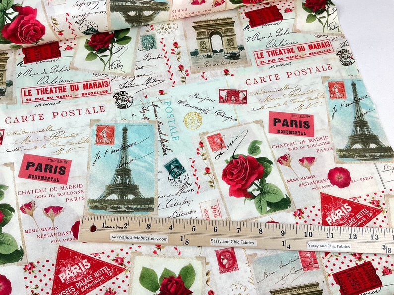 Może przedstawiać: Tkanina z motywem vintage paryskiej poczt&oacute;wki. Tkanina zawiera obrazy Wieży Eiffla, Łuku Triumfalnego i czerwonych r&oacute;ż. Tekst zawiera "Carte Postale" i "Paris Monumental".