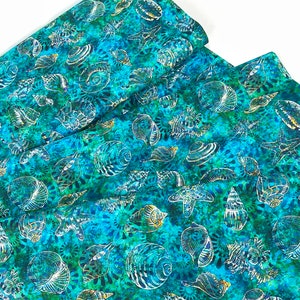 May include: A folded fabric with a repeating pattern of white seashells and starfish on a teal and turquoise background. The fabric has a batik-like appearance with gold accents, creating a coastal theme.