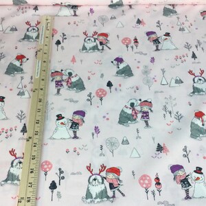 May include: Pink fabric with a winter-themed pattern. The design features illustrations of children, snowmen, dogs, and trees. The fabric is decorated with a ruler for measurement.