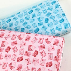 May include: Two fabric bolts, one light blue and one pink, are patterned with watercolor-style envelopes. The envelopes have a button closure and the number "3" printed on them. The fabric is likely cotton or a similar material.