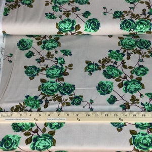 May include: Fabric with a floral pattern of green roses and brown stems on a light gray background. The fabric is folded over, showing the edge of the roll. A ruler is placed on the fabric for measurement.
