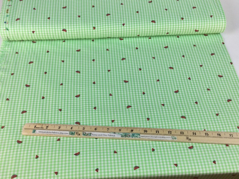 K&ouml;nnte beinhalten: Gr&uuml;n-wei&szlig;es Vichy-Stoff mit verstreuten Wassermelonen-Scheiben-Designs. Ein Holzlineal mit Zollma&szlig;en liegt auf dem Stoff. Der Stoff ist im Hintergrund aufgerollt.