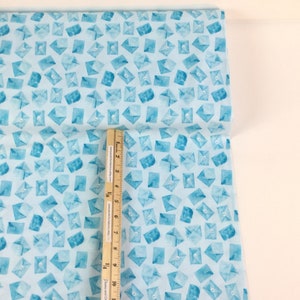 May include: Light blue fabric with a repeating pattern of watercolor-style envelopes. The envelopes are in shades of blue and have a button detail. A ruler is placed on the fabric, showing inches.