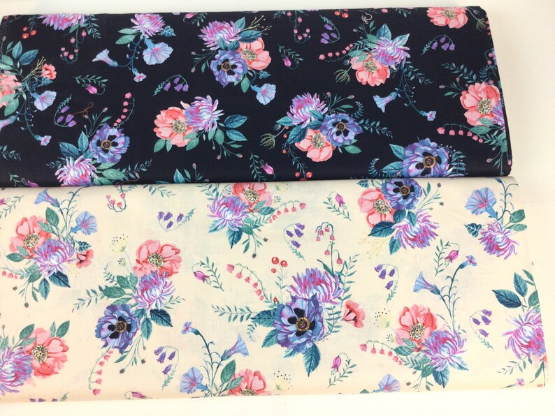 May include: Two rolls of floral fabric. One is navy blue, the other is cream. Both feature a repeating pattern of pink, purple, and blue flowers with green leaves. The fabric is likely cotton or a similar material.