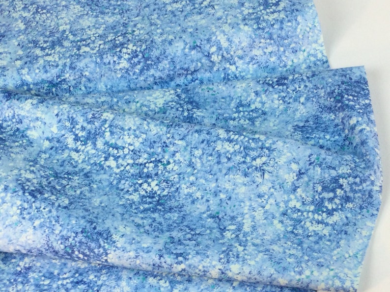 May include: A close-up of a fabric with a blue and white floral pattern. The fabric has a soft, textured appearance with a watercolor effect. The color palette includes shades of blue and white.