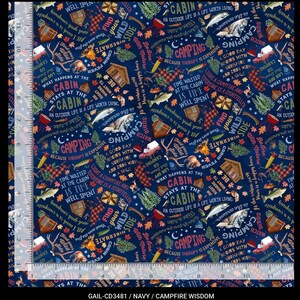 May include: Navy blue fabric featuring a camping theme. The design includes cabins, fish, deer, trees, and text like "Camping" and "Find Your Wild Side." The fabric also has a ruler along the left side.