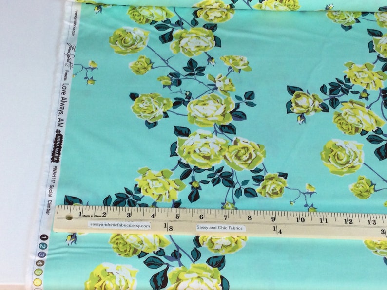 May include: A fabric with a light blue background featuring a floral pattern of yellow roses and dark green leaves. The fabric includes the text "Love Always, AM" and "Sassy and Chic Fabrics". A ruler shows measurements in inches.