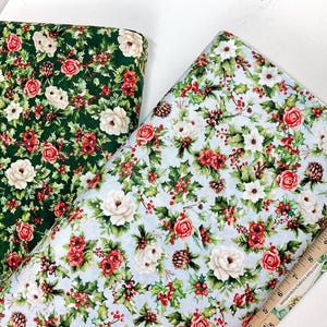 K&ouml;nnte beinhalten: Zwei Stoffrollen mit floralen Mustern. Eine hat einen dunkelgr&uuml;nen Hintergrund mit roten und wei&szlig;en Rosen, Stechpalmen und Tannenzapfen. Die andere hat einen hellblauen Hintergrund mit dem gleichen floralen Design. Rechts ist ein Holzlineal.