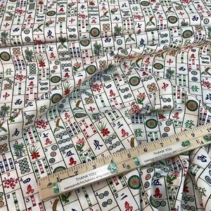 May include: White fabric with a repeating pattern of Mahjong tiles in red, green, and black. A wooden ruler with the text "THANK YOU sassyandchicfabrics.etsy.com" is placed on the fabric. The fabric is folded.