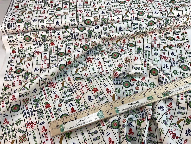 May include: White fabric with a repeating pattern of Mahjong tiles in red, green, and black. A wooden ruler with the text "THANK YOU sassyandchicfabrics.etsy.com" is placed on the fabric. The fabric is folded.