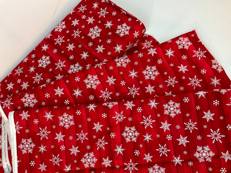 Pu&ograve; includere: Tessuto rosso con un motivo a fiocchi di neve bianchi. Il tessuto ha una trama a venature di legno ed &egrave; piegato a strati. I fiocchi di neve variano per dimensioni e design, creando un tema invernale festoso.
