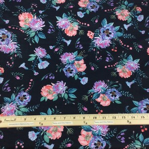 May include: Dark navy fabric with a repeating floral pattern. The design features clusters of pink, purple, and blue flowers with green foliage. A ruler with inch measurements is visible.