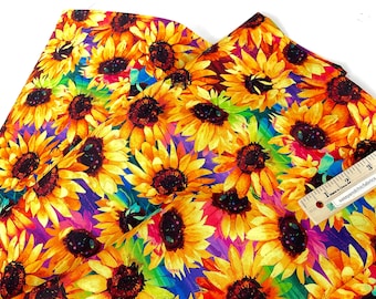 May include: Vibrant fabric featuring a repeating pattern of sunflowers in full bloom. The sunflowers have yellow petals and dark brown centers, set against a colorful background of purple, blue, and green. A ruler is included for scale.
