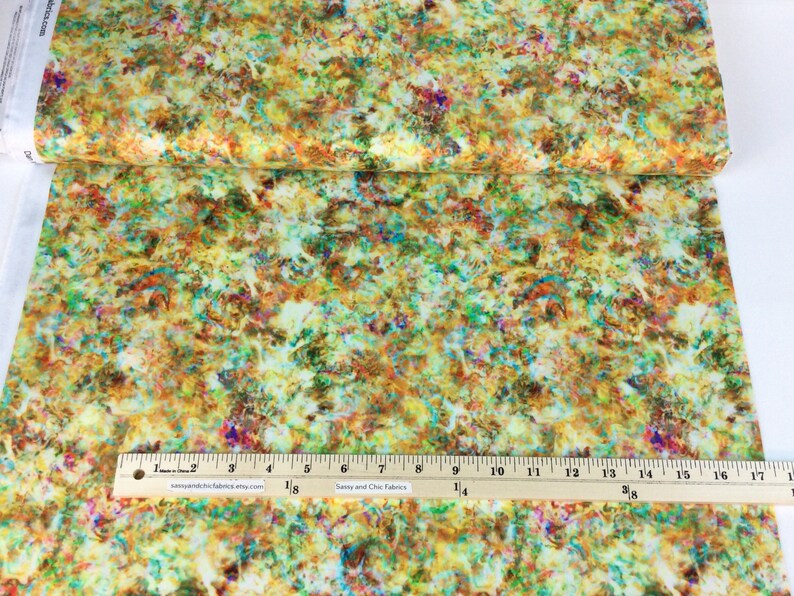 May include: Fabric with a colorful abstract design. The fabric features a mix of yellow, green, orange, and purple hues. A ruler with inch measurements is placed on the fabric. The text "Sassy and Chic Fabrics" is visible.