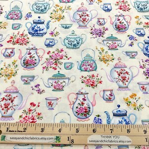 May include: Fabric with a repeating pattern of teapots, teacups, and floral arrangements in shades of blue, pink, and green on a cream background. The fabric includes a ruler with measurements in inches and the text "sassyandchicfabrics.etsy.com".