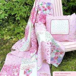 May include: A pink and white floral quilt and matching pillow with an "XOX" design. The quilt features various floral patterns and is draped over a pink chair. The pillow is square and has a stitched border. The quilt is made of cotton.