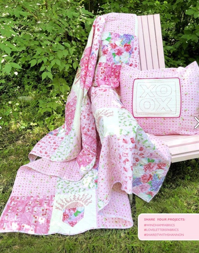May include: A pink and white floral quilt and matching pillow with an "XOX" design. The quilt features various floral patterns and is draped over a pink chair. The pillow is square and has a stitched border. The quilt is made of cotton.