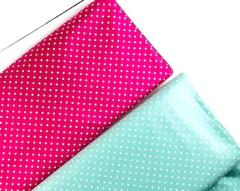 May include: Two fabric pieces, one hot pink and the other aqua, are visible against a white background. Both fabrics are patterned with small, evenly spaced white polka dots. The fabrics are folded and angled, creating a dynamic composition.