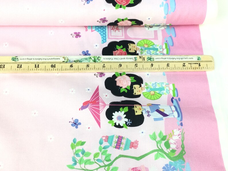 May include: Pink fabric with a repeating pattern of Japanese geishas, flowers, and lanterns. The design includes geishas with black hair, holding fans and umbrellas. The fabric is decorated with butterflies and small white flowers.