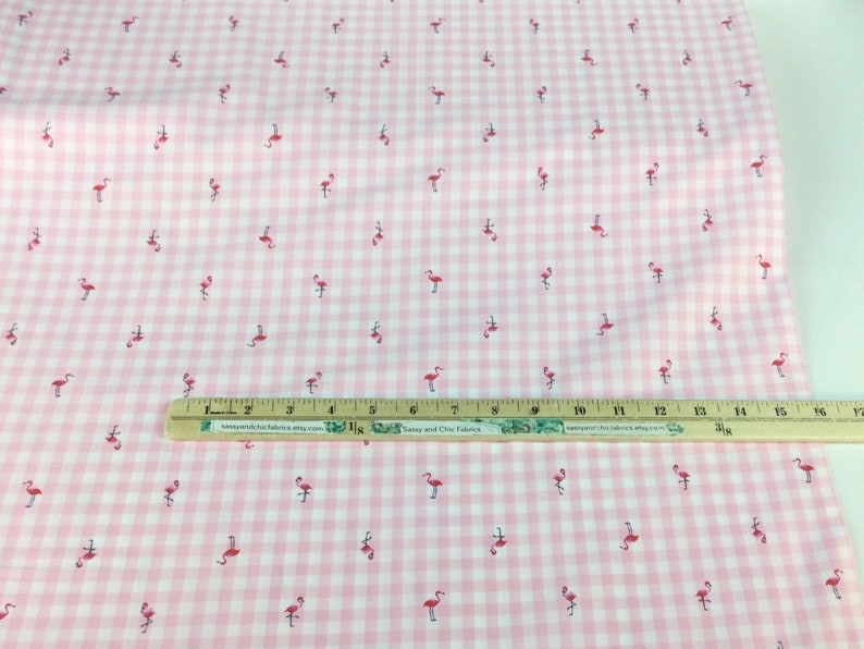 Puede incluir: Tela de cuadros rosa y blanco con un estampado de peque&ntilde;os flamencos rosas. Una regla de madera con medidas en pulgadas est&aacute; colocada sobre la tela. La tela es adecuada para proyectos de costura y manualidades.