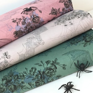 Puede incluir: Tres rollos de papel decorativo en rosa, crema y verde azulado, con ilustraciones florales y de murci&eacute;lagos y telara&ntilde;as. Hay ara&ntilde;as de pl&aacute;stico negro esparcidas alrededor de los rollos, lo que sugiere un tema de Halloween. El papel es adecuado para manualidades y envolver regalos.