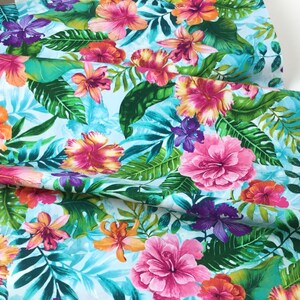 May include: Vibrant fabric featuring a tropical floral pattern. The design showcases large pink, orange, and purple hibiscus flowers, lush green leaves, and a light blue background. This fabric is ideal for creating apparel or home decor items.