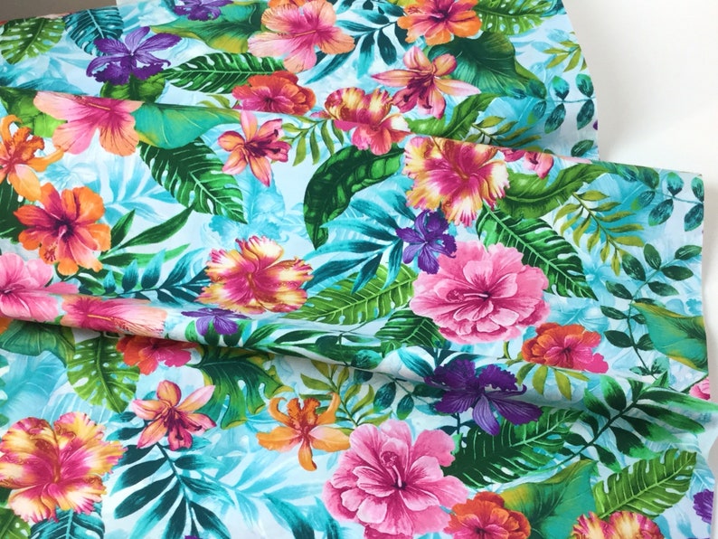 May include: Vibrant fabric featuring a tropical floral pattern. The design showcases large pink, orange, and purple hibiscus flowers, lush green leaves, and a light blue background. This fabric is ideal for creating apparel or home decor items.