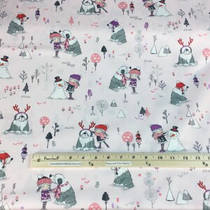 May include: Pink fabric with a winter scene featuring children, snowmen, and Old English Sheepdogs. The design includes trees, mountains, and decorative elements in shades of gray, pink, and purple. A ruler is placed on the fabric.