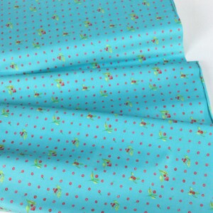 Puede incluir: Tela turquesa con un patr&oacute;n repetido de cerezas rojas y hojas verdes. La tela est&aacute; doblada, mostrando la textura y el dise&ntilde;o. Ideal para proyectos de acolchado, costura o manualidades.