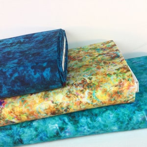 May include: Three rolls of fabric with vibrant, abstract patterns. One roll is a deep teal, while the others display a mix of yellow, orange, and teal hues. The fabrics appear to have a marbled or watercolor effect.