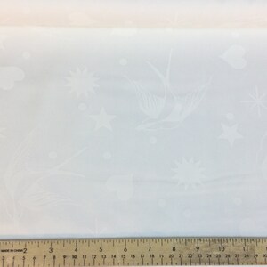 May include: White fabric with an embossed pattern featuring birds, stars, hearts, and dots. The fabric is measured with a ruler. The design is delicate and suitable for various craft projects.