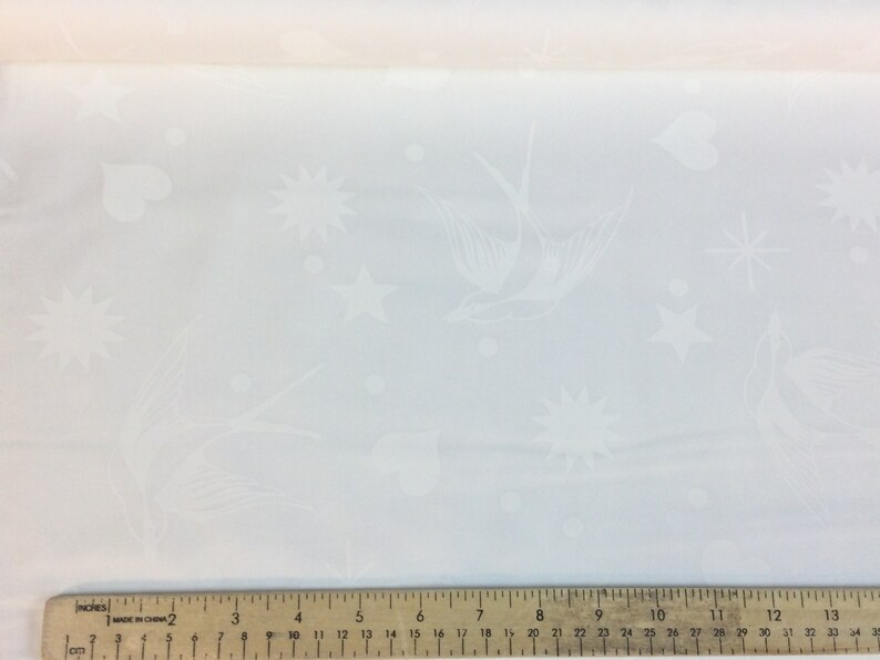 May include: White fabric with an embossed pattern featuring birds, stars, hearts, and dots. The fabric is measured with a ruler. The design is delicate and suitable for various craft projects.