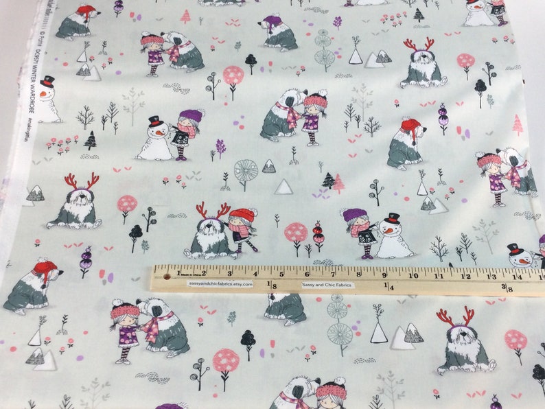May include: Light gray fabric with a winter-themed pattern. The design features illustrations of children, snowmen, dogs, trees, and mountains in shades of gray, pink, and purple. The fabric is suitable for various sewing projects.