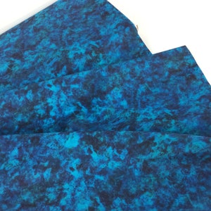 May include: Folded fabric with a vibrant, abstract pattern in shades of teal, turquoise, and deep blue. The design resembles a watercolor effect or a marbled appearance. The fabric is likely used for sewing or crafting projects.